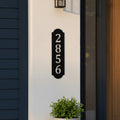 Gloss black vertical metal house number sign mounted beside a front door on a white exterior wall