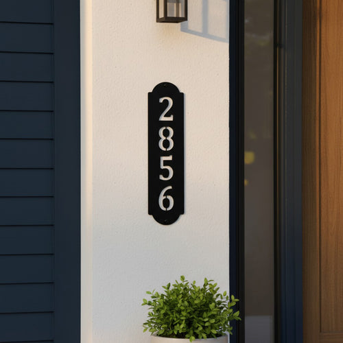 Gloss black vertical metal house number sign mounted beside a front door on a white exterior wall