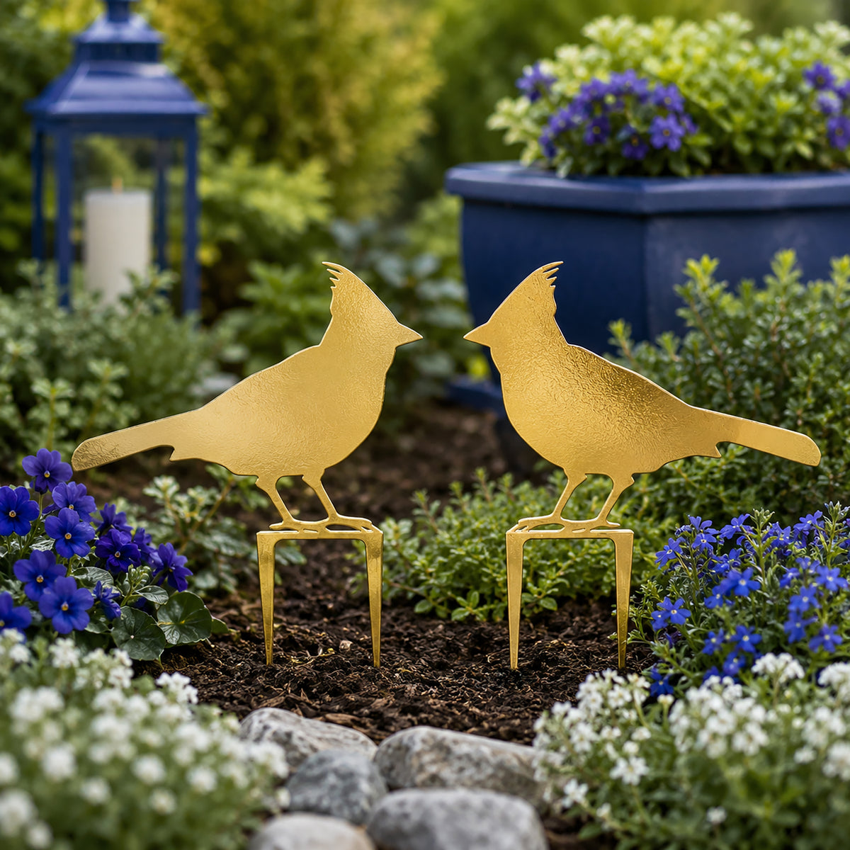 Gold cardinal metal garden stakes displayed in a flower bed with blue and white blooms for outdoor garden decor