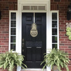 Gold pineapple welcome door decor displayed on black front door with brick porch and green plants
