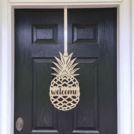 Gold pineapple welcome front door hanger shown close up on black door for tropical entryway decor