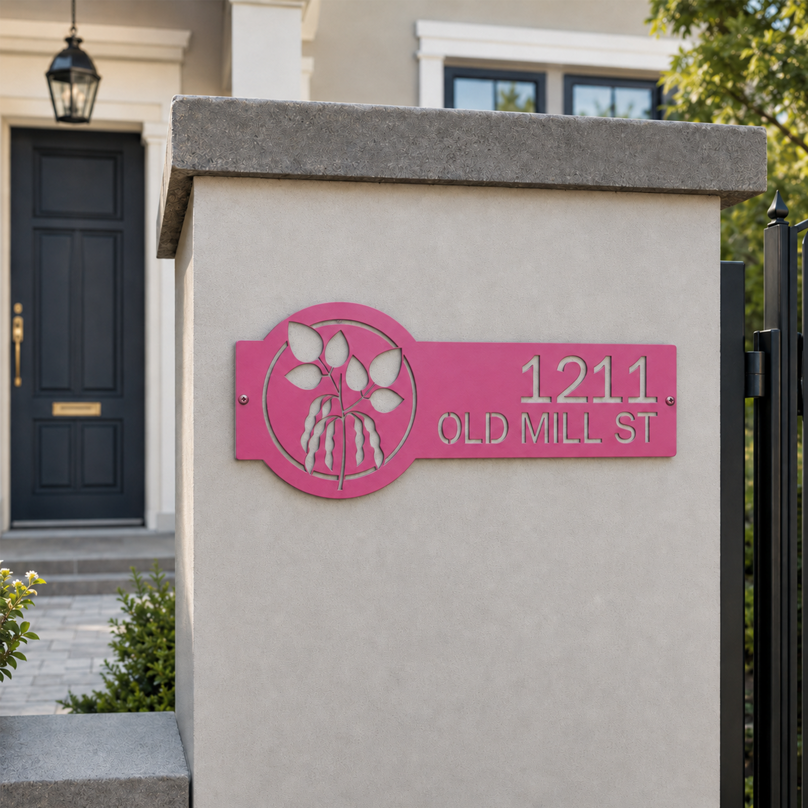 Hot pink custom metal house address plaque with botanical leaf design mounted on outdoor concrete pillar displaying 1211 Old Mill St