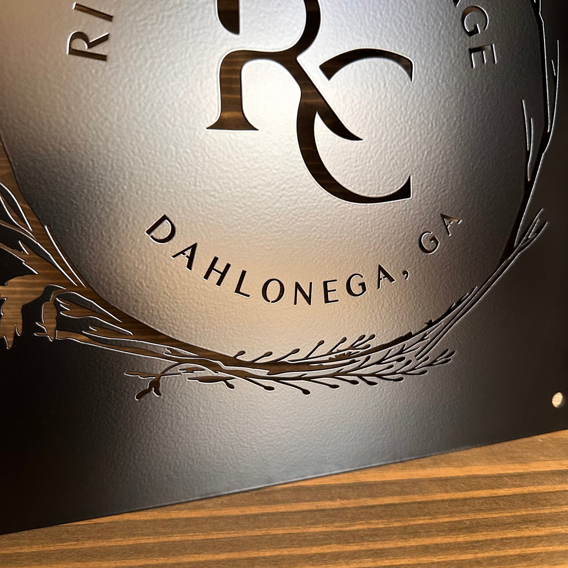 Close-up of laser-cut steel sign with “DAHLONEGA, GA” on curved edge, leaf accents, and textured metallic finish.
