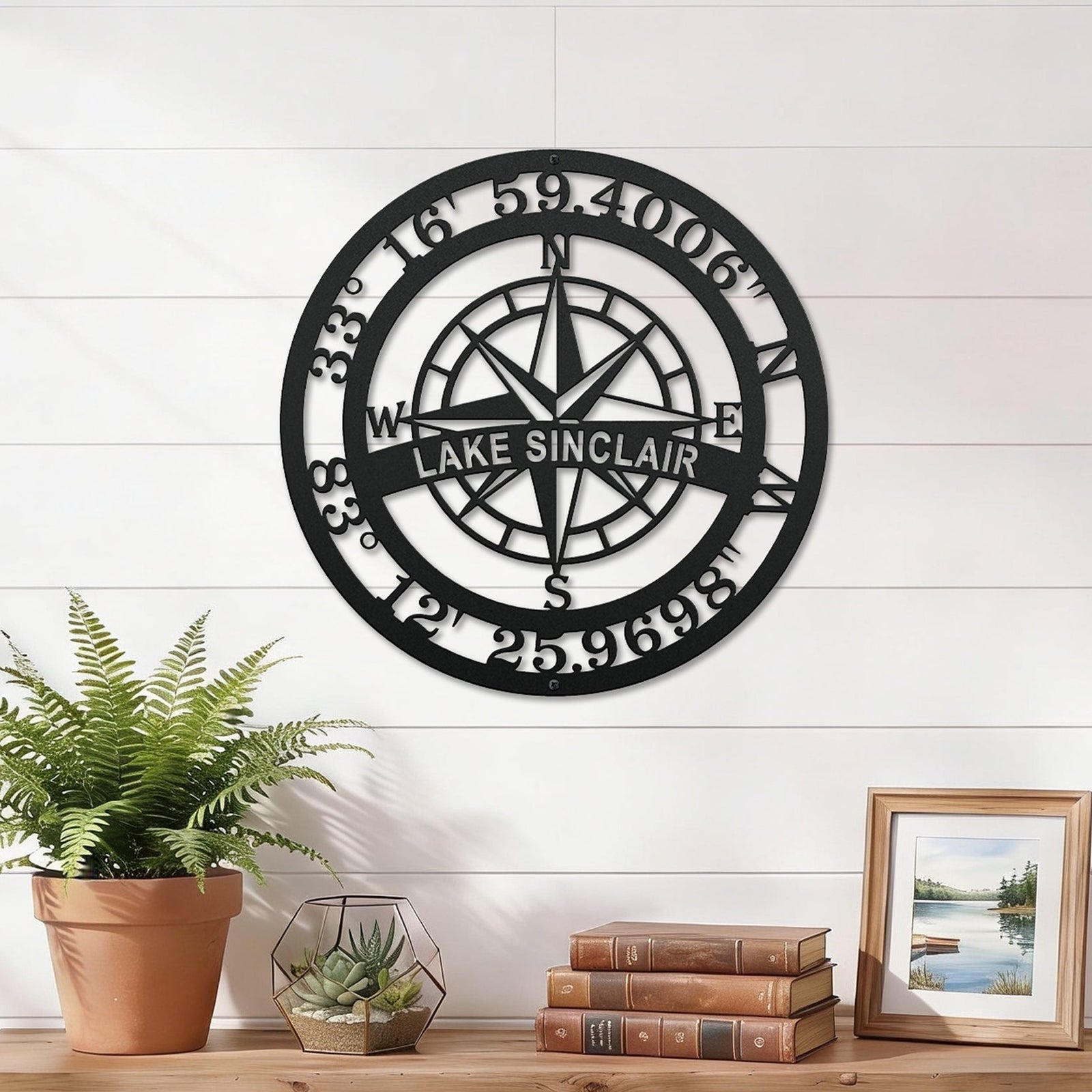Custom Lake Sinclair compass coordinates metal wall sign displayed above wooden shelf with books plants and framed lake artwork