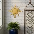 A gold-colored metallic sunburst sign hung on a white brick interior wall, positioned between a large window and a decorative brown iron trellis above a potted green fern.