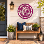 Magenta custom family name metal wall art with sun and tree design displayed above a rustic front porch bench with decorative pillows
