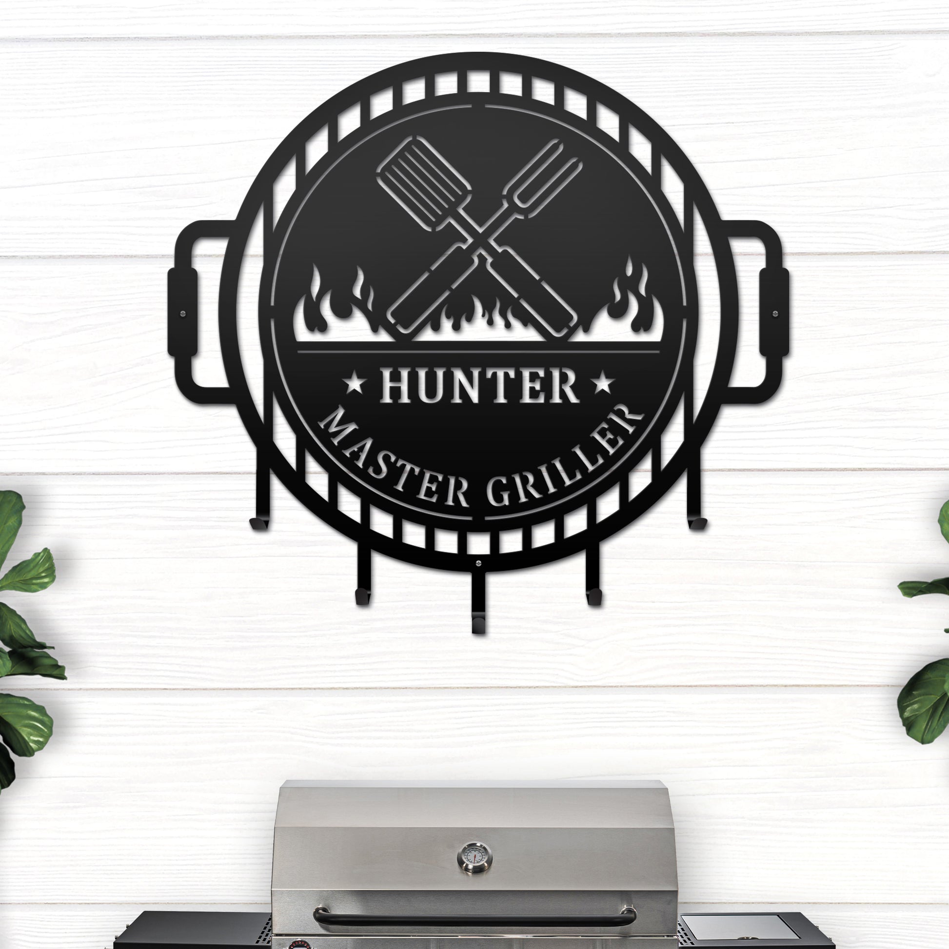 Grill Master Name Sign with Metal Hooks featuring a black circular design with crossed spatulas and fire logo, ideal for organizing grilling utensils in outdoor kitchens or man caves.