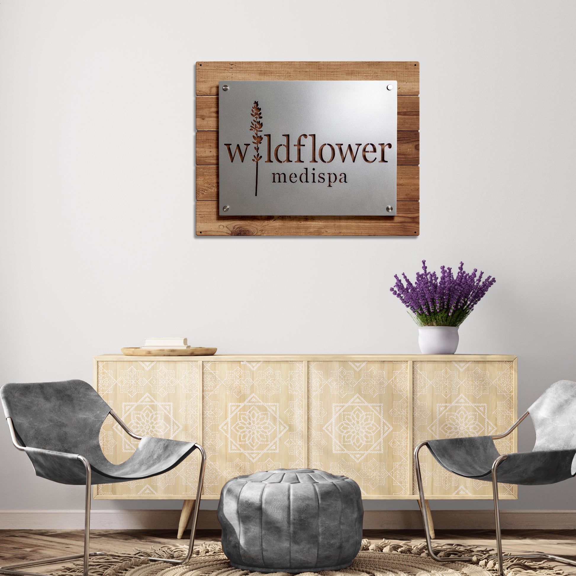 RM Custom Size Test metal business logo sign displayed on a wooden surface, alongside a grey round leather ottoman and purple flowers in a vase, highlighting its professional appeal.