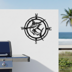 Matte black metal marlin compass wall sign mounted on a modern white patio wall next to an outdoor barbecue grill overlooking the ocean.