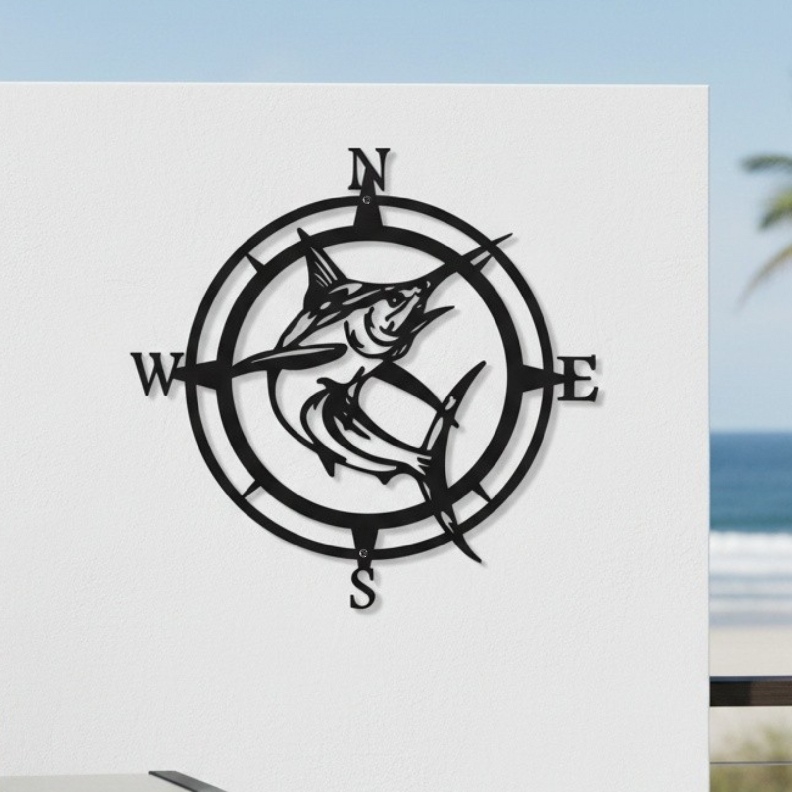 Matte black metal marlin compass wall sign mounted on a modern white patio wall next to an outdoor barbecue grill overlooking the ocean.
