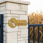 Metallic gold corn address sign with 1211 Old Mill St mounted on a white stone pillar beside a cornfield