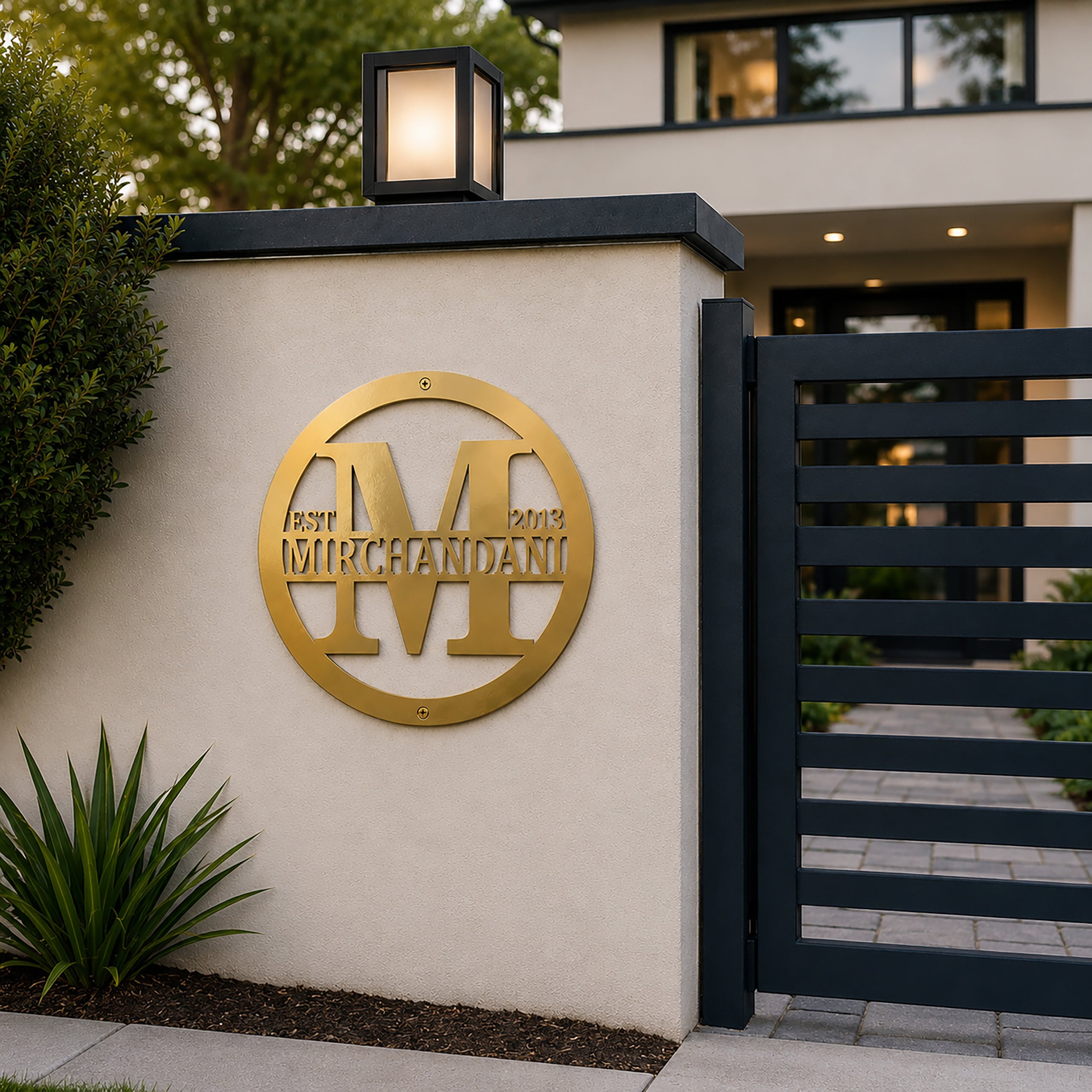 Metallic gold personalized family name monogram sign mounted on an outdoor entry wall beside a modern gate