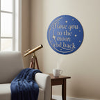 Textured satin black circular metal text sign mounted on an off-white wall above a minimalist wooden bench decorated with dried pampa grass in a black vase.