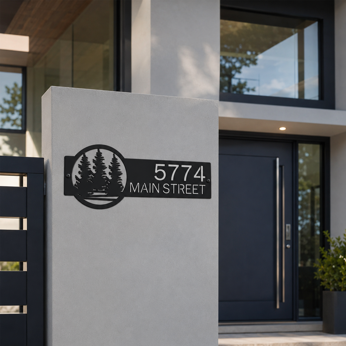 Contemporary black custom address plaque with pine tree landscape design mounted on concrete front entry wall displaying 5774 Main Street