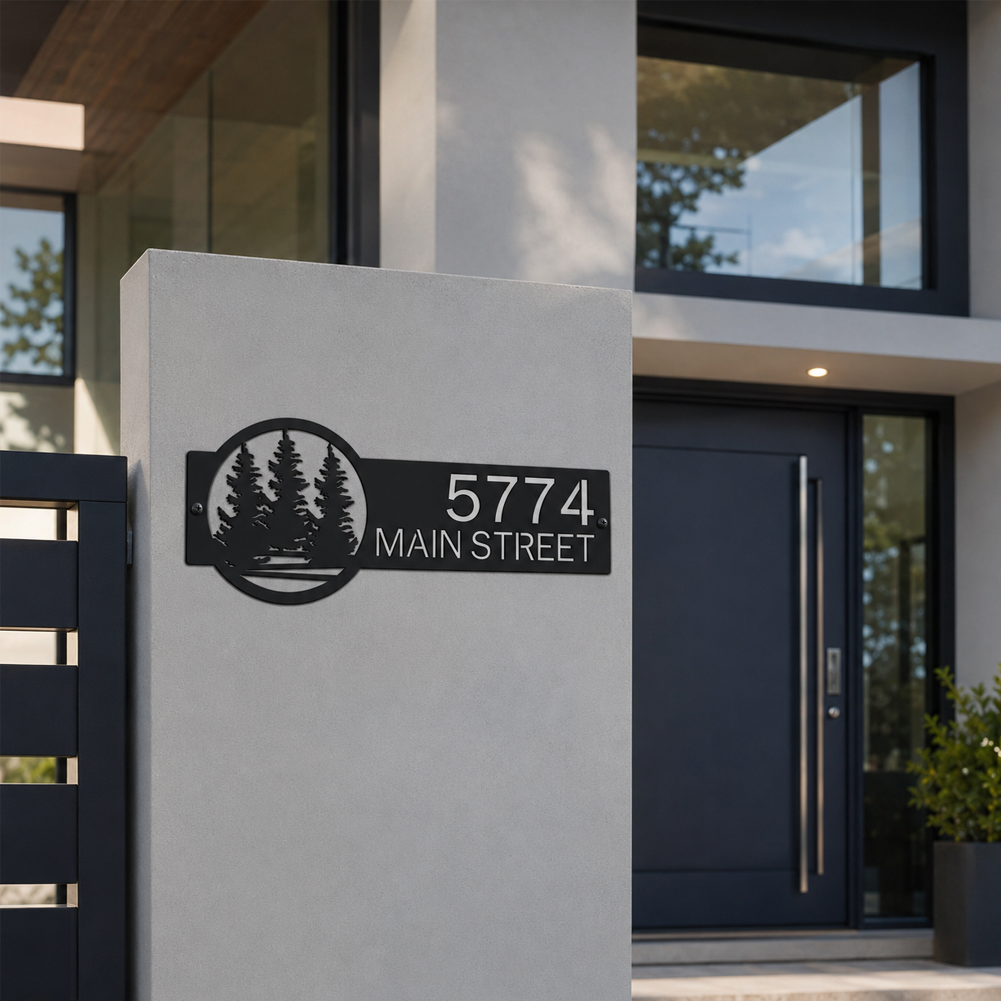 Contemporary black custom address plaque with pine tree landscape design mounted on concrete front entry wall displaying 5774 Main Street