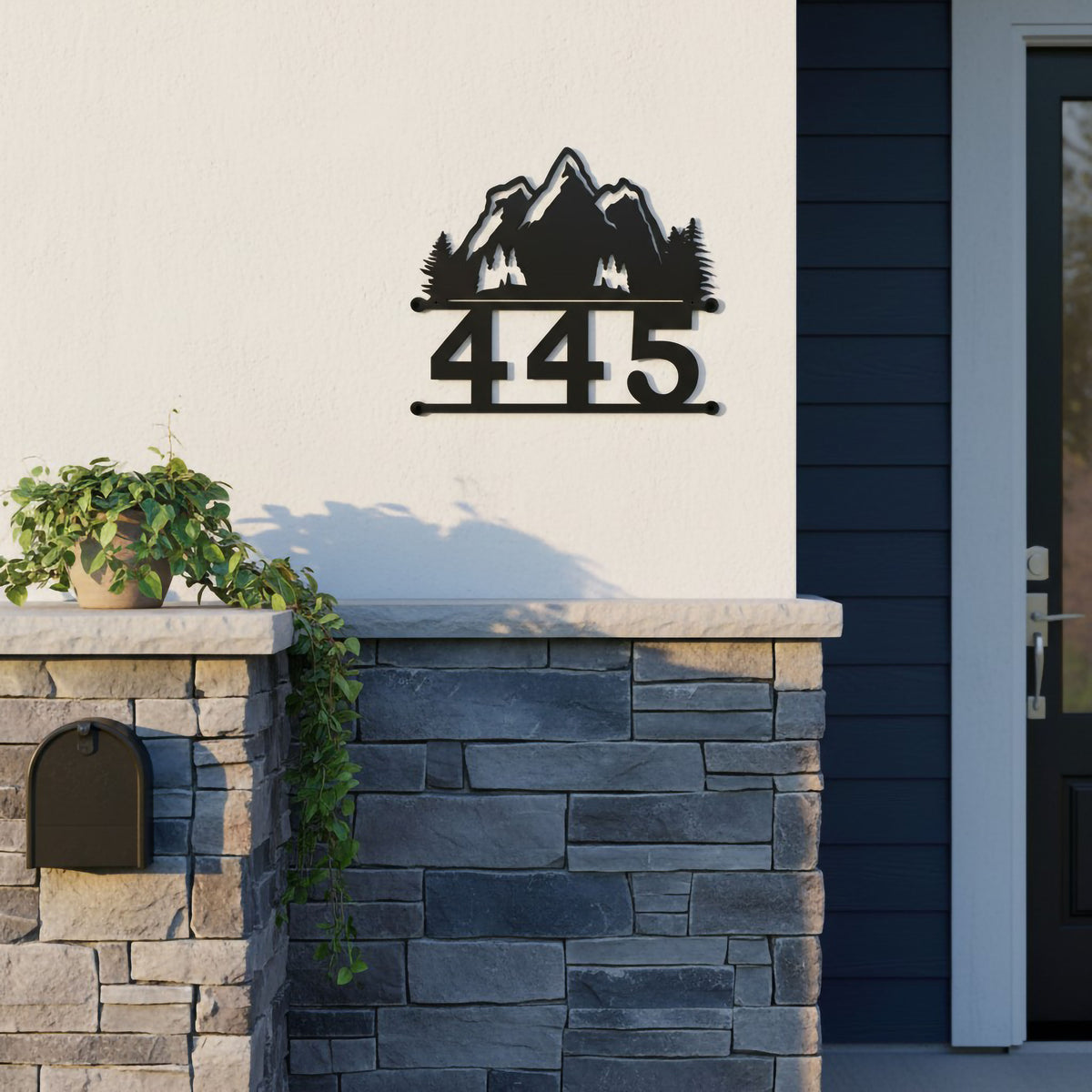 Black mountain metal address plaque with 445 displayed on white exterior wall above stone accent siding