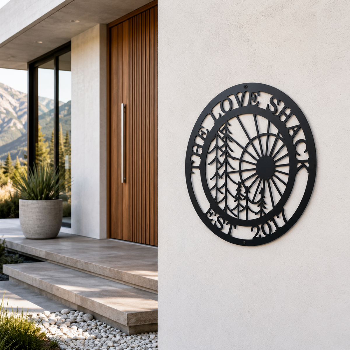 Black circular personalized metal wall art sign with sunburst and pine tree design mounted outside a modern luxury home entrance