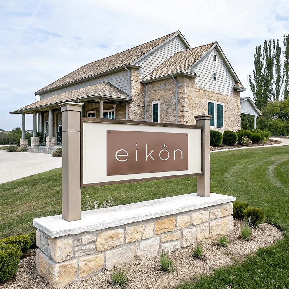 Contemporary outdoor business monument sign with stone base and modern panel display positioned in front of commercial office building with landscaped lawn and walkway