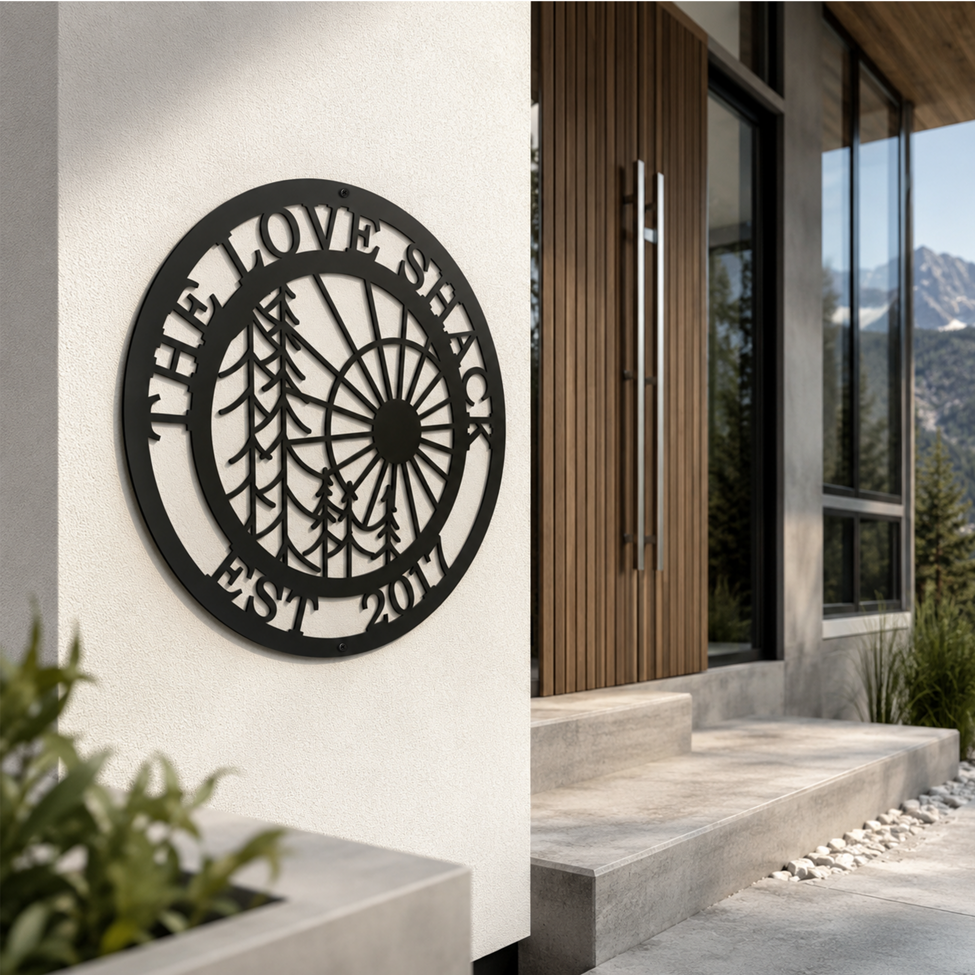 Black custom family metal wall sign with forest and sun design displayed on a modern outdoor stucco wall beside a wooden front door