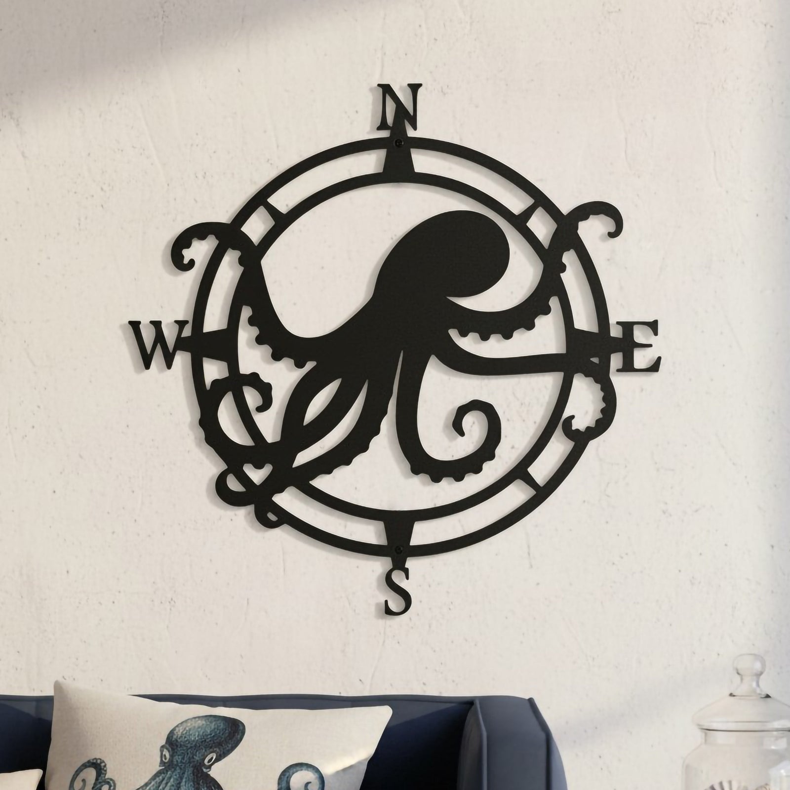Black octopus compass metal wall art displayed above a sofa with nautical pillows and shell décor