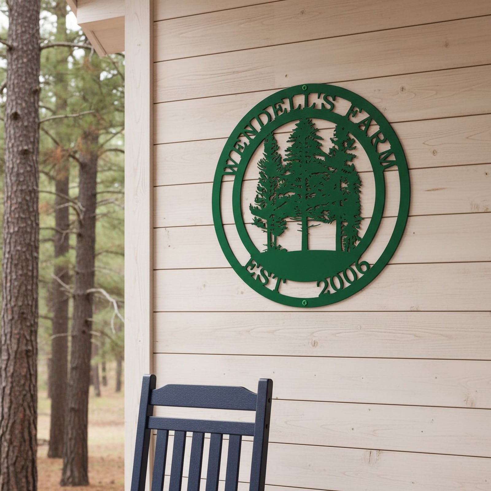A green round metal custom sign with a pine forest graphic reading "Wendell's Farm Est. 2006," mounted on light wood horizontal siding behind a dark blue rocking chair.