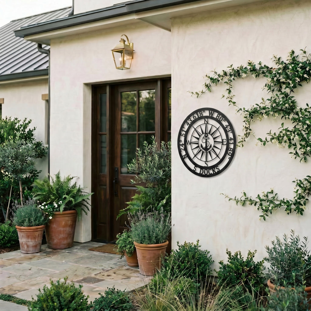 Personalized compass metal wall art displayed on exterior stucco wall with greenery and modern outdoor decor