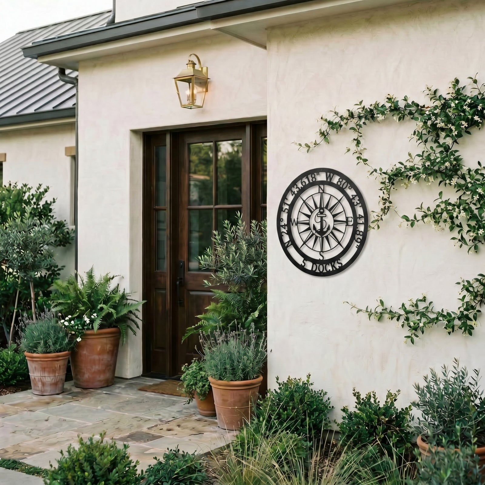 Personalized compass metal wall art displayed on exterior stucco wall with greenery and modern outdoor decor