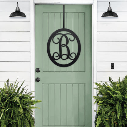 Classy Classic Oval Monogram Door Wreath hangs elegantly on a green door, showcasing a personalized black metal monogram. Ideal for home entrances, blending timeless design with customizable features.