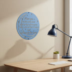 Light blue finish of the custom circular lyrical metal plaque mounted on a warm beige wall behind a wooden computer desk with a dark blue lamp.