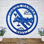 Custom round aviation metal sign featuring airplane silhouette clouds and personalized hangar name with aircraft registration number displayed on white brick wall background