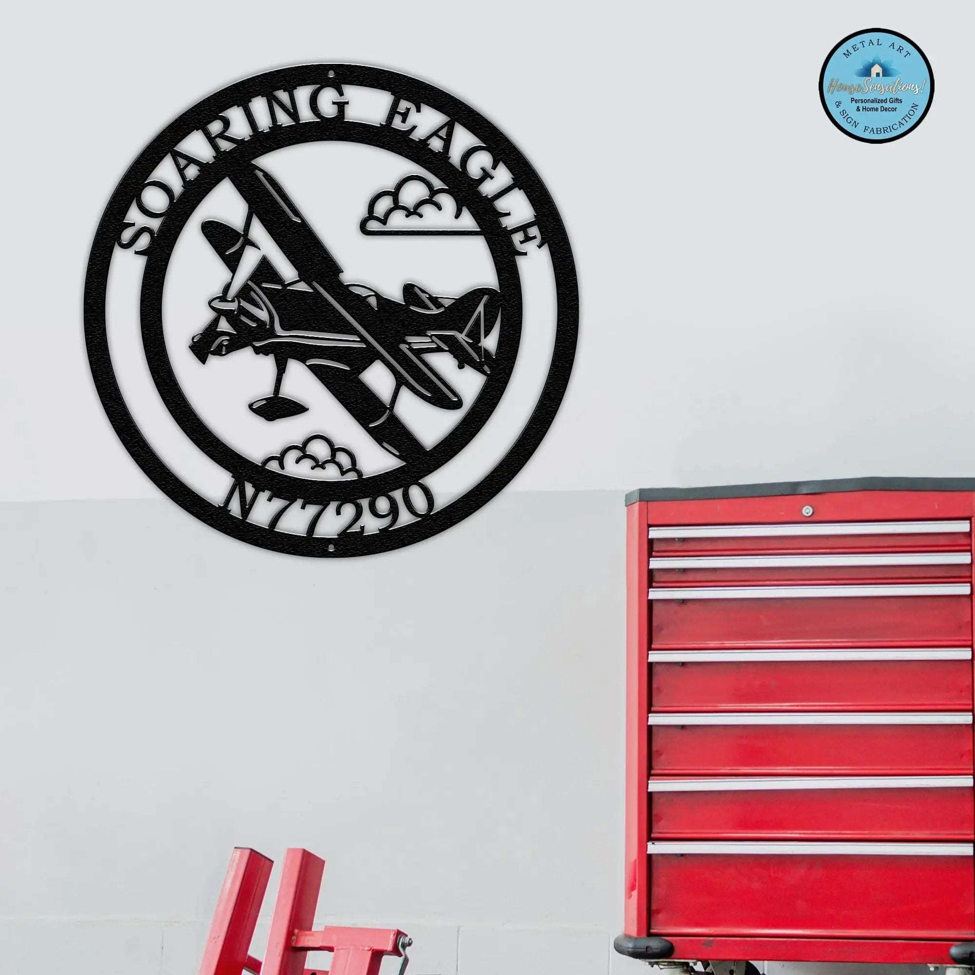 Custom aviation metal wall sign featuring airplane silhouette and personalized hangar name with aircraft registration number displayed in workshop garage with red tool cabinet background