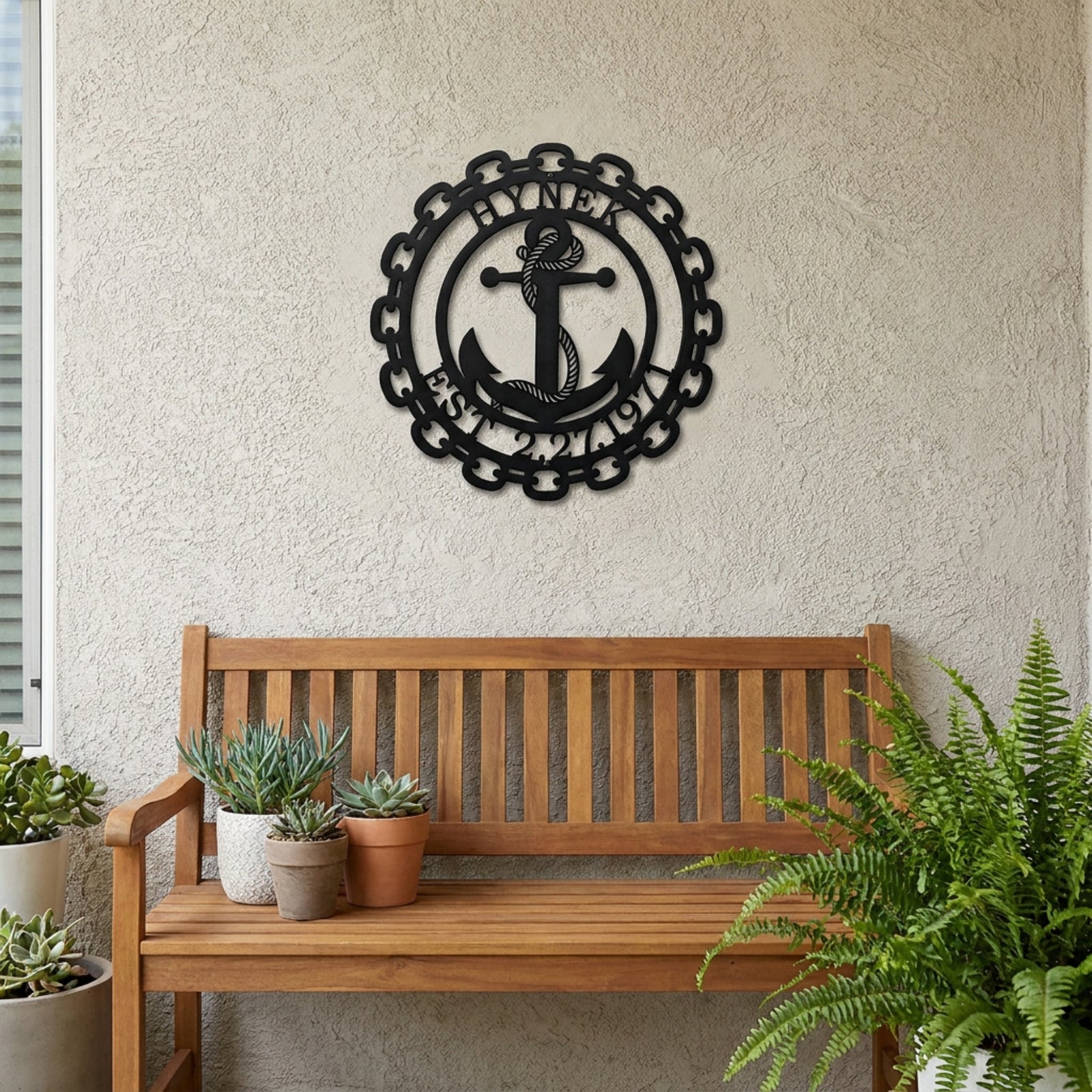Black personalized anchor monogram metal sign with family name and established date displayed above wooden bench on outdoor patio wall