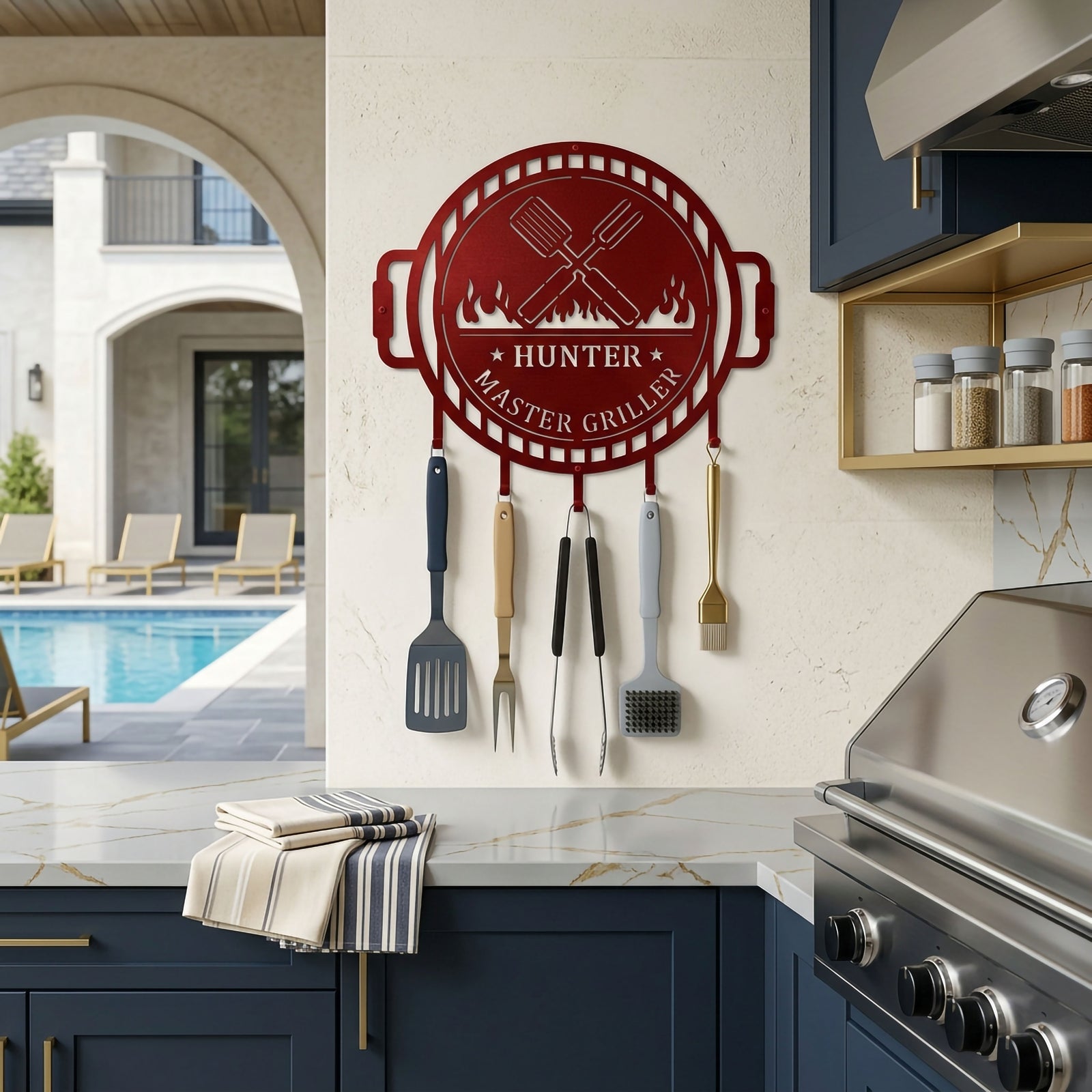 Red personalized BBQ tool rack metal wall decor displayed in luxury outdoor kitchen beside grilling station and cooking utensils
