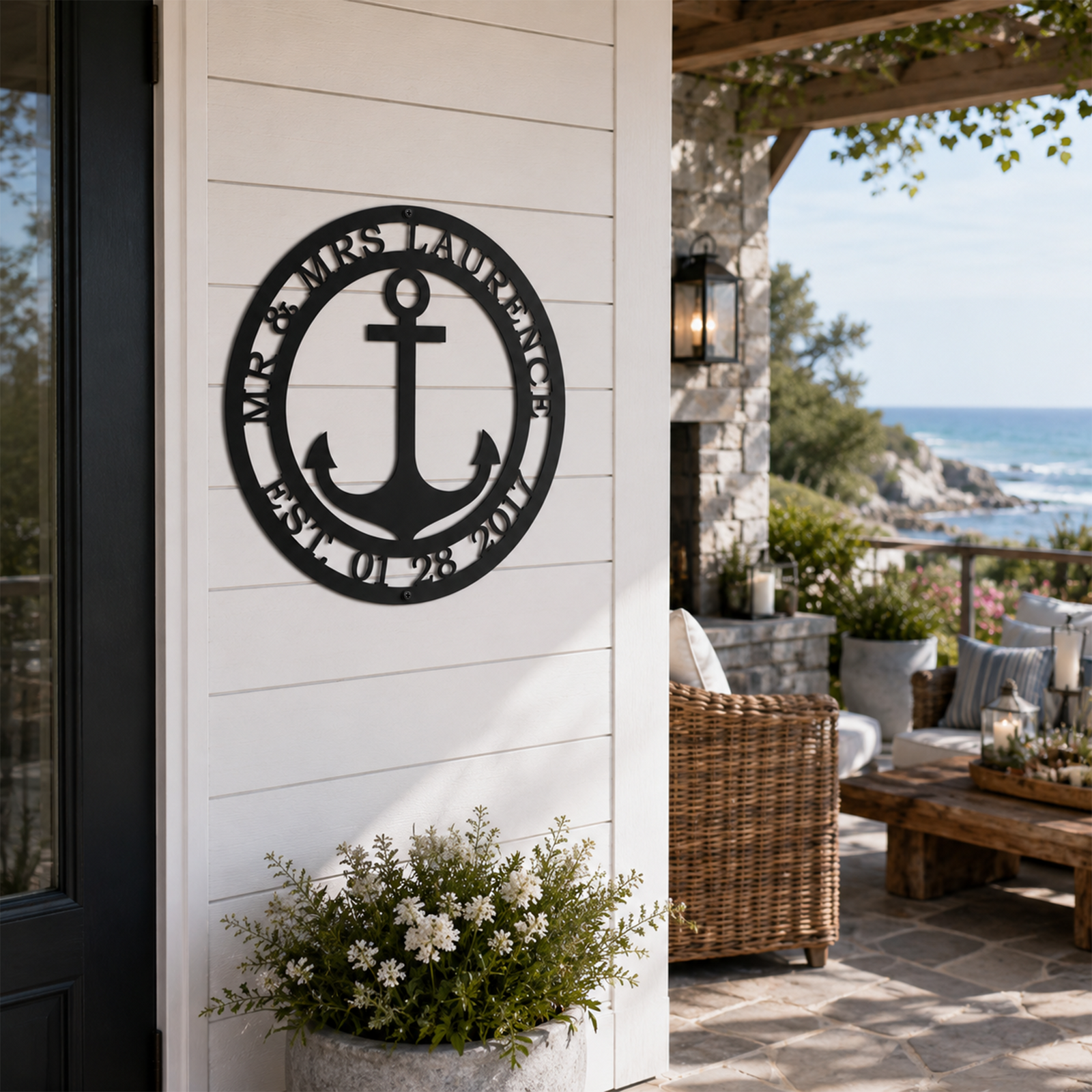 Satin black custom circular anchor metal sign mounted on a white exterior wall above a potted white flower arrangement next to a porch seating area.