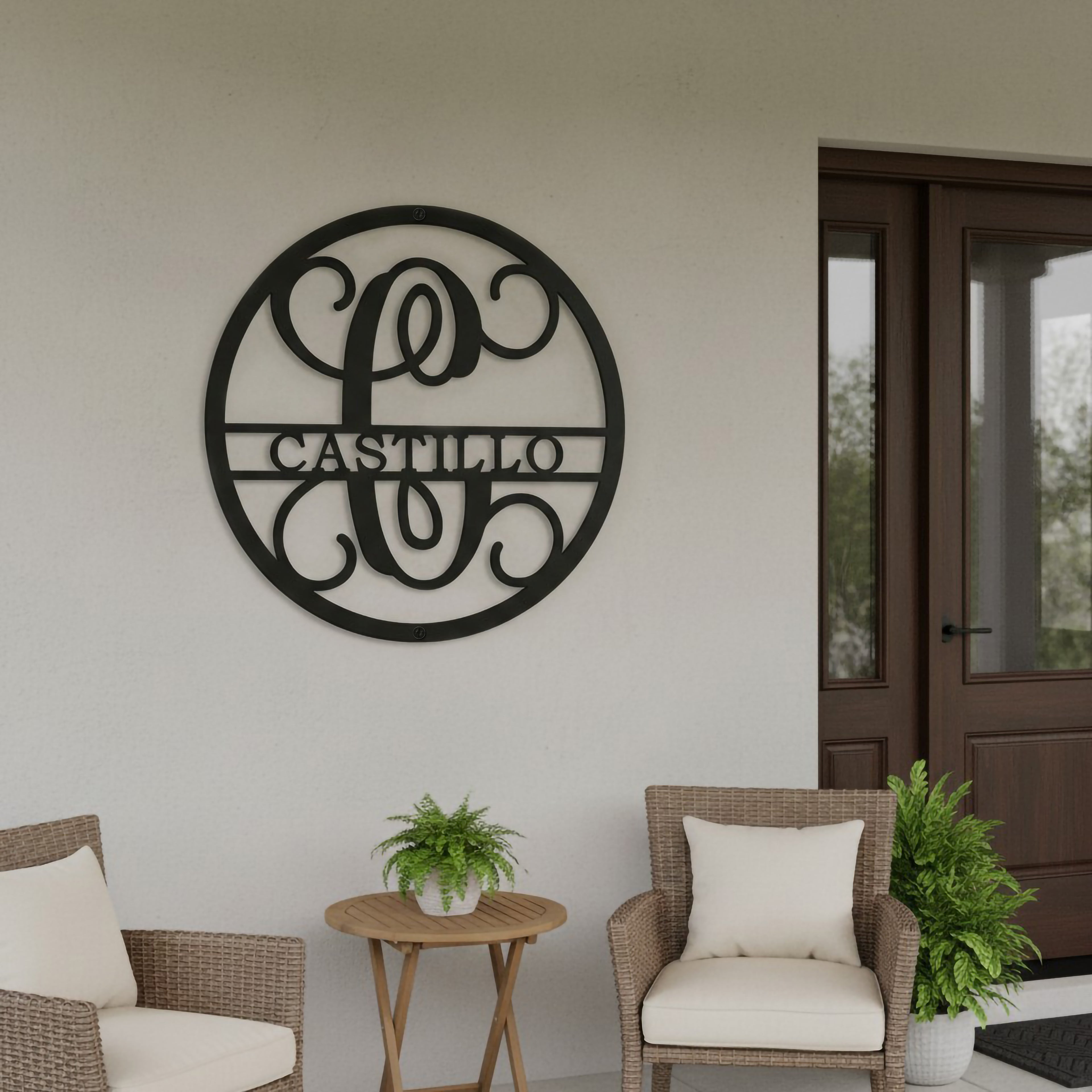 Satin black custom family name metal plaque featuring a split letter monogram mounted on a white porch wall above cozy outdoor wicker seating.