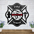 Black Maltese cross metal sign with a thin red line and custom name on a white brick wall above a wood shelf.