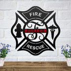 Black Maltese cross metal sign with a thin red line and custom name on a white brick wall above a wood shelf.