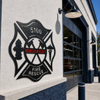 Personalized black and red firefighter Maltese Cross metal sign displayed outside fire station with fire truck in background