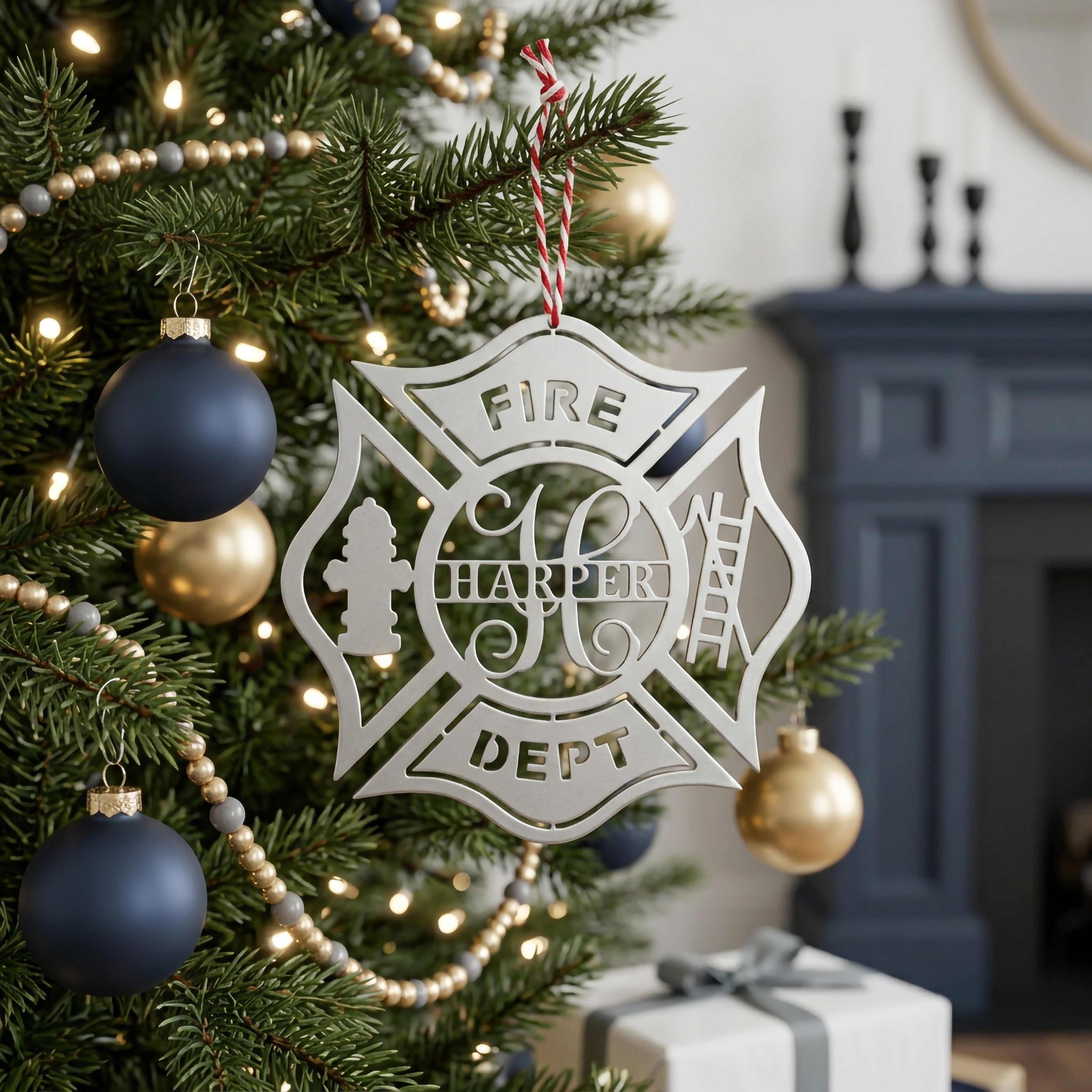 Silver firefighter maltese cross Christmas ornament with custom Harper name hanging on decorated holiday tree with navy and gold ornaments