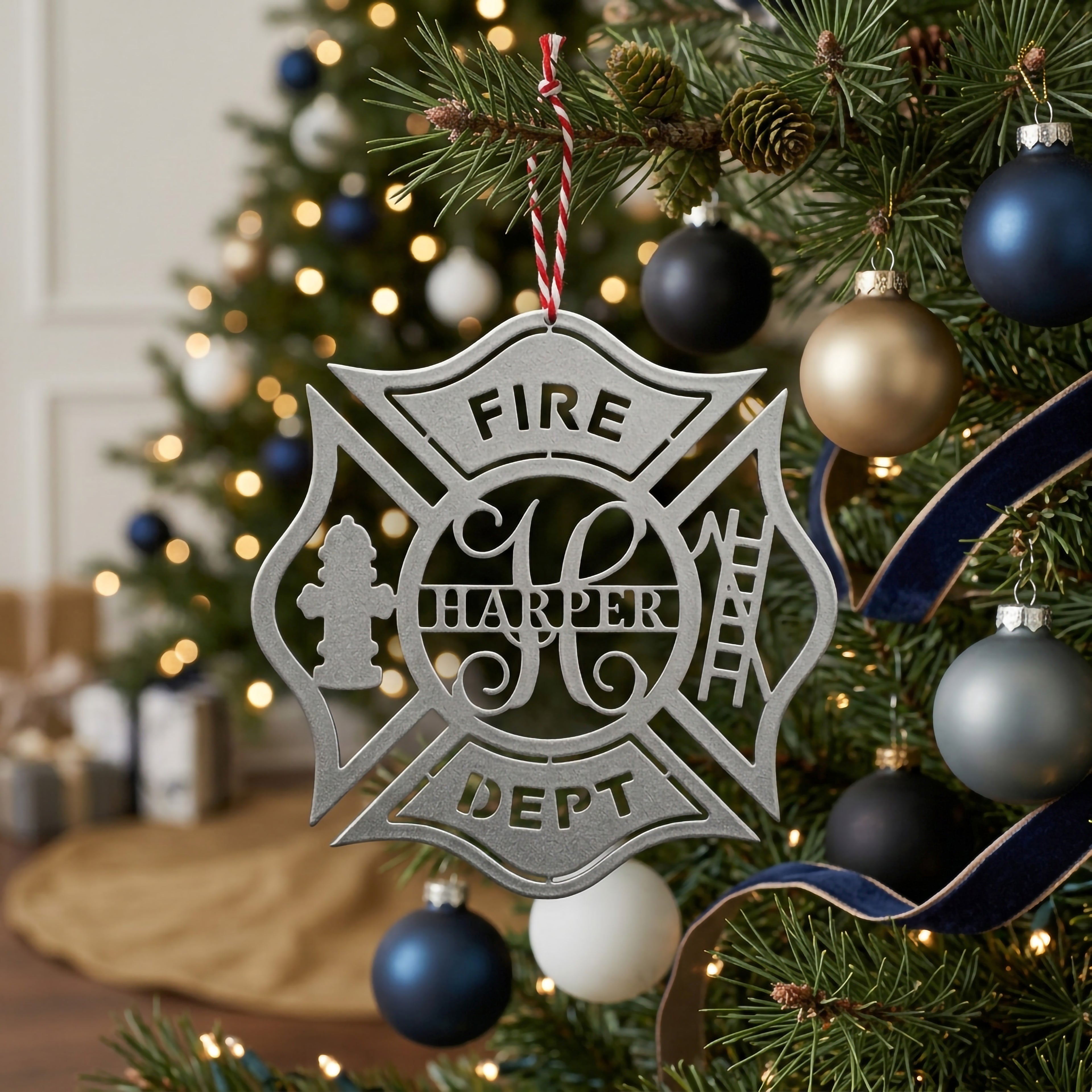 Custom silver firefighter ornament with Harper name hanging on Christmas tree branch with blue gold and white ornaments