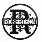 Flat view of a black circular personalized metal sign with a large letter R monogram and decorative scrollwork cut out with the family name Robertson over a pure white background.