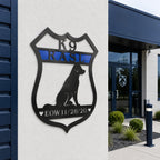 Black personalized K9 memorial badge metal sign with blue stripe mounted on an exterior wall outside a K9 facility entrance