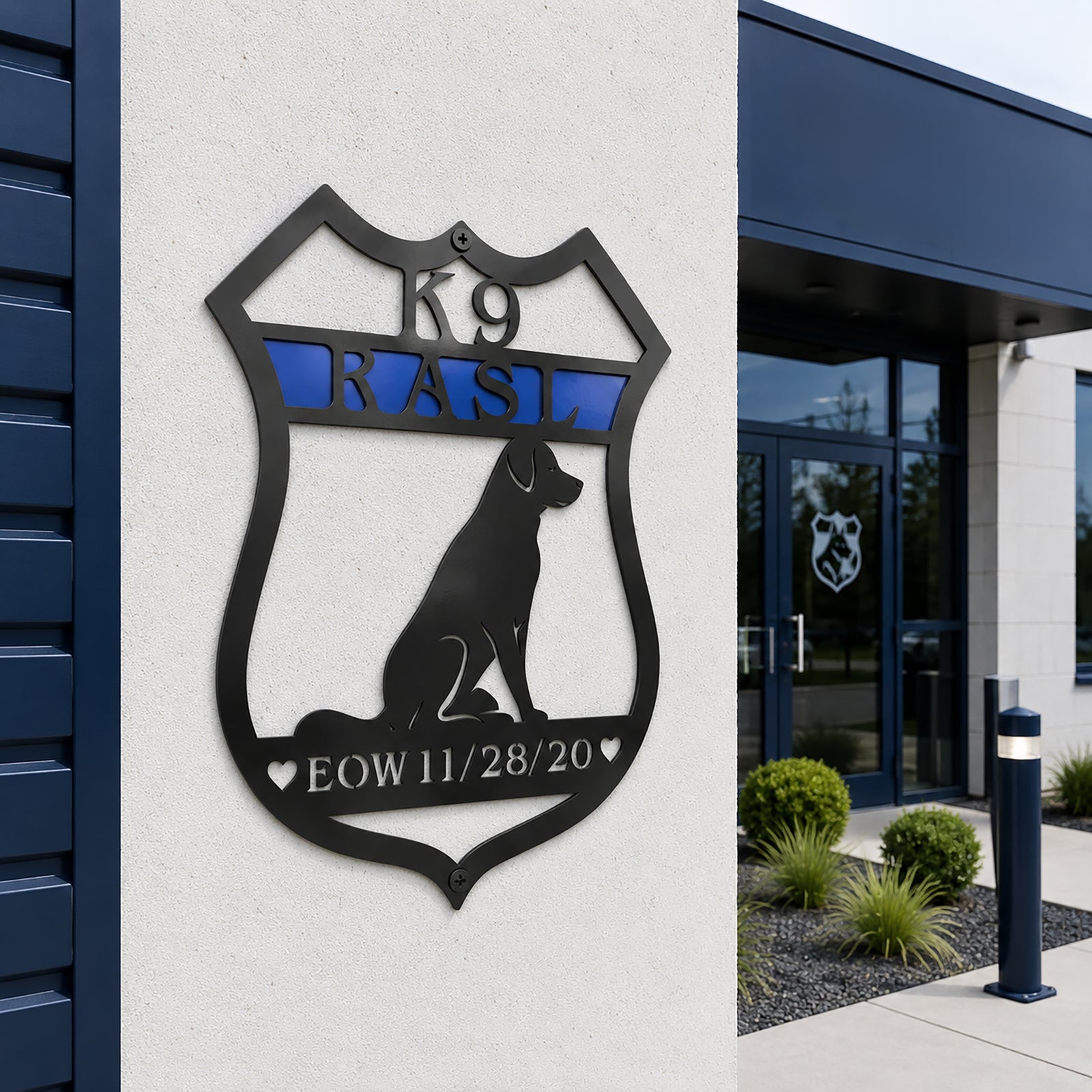 Black personalized K9 memorial badge metal sign with blue stripe mounted on an exterior wall outside a K9 facility entrance