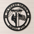 Personalized lineman metal wall sign featuring utility worker climbing power pole with American flag custom years and service company name in black steel décor