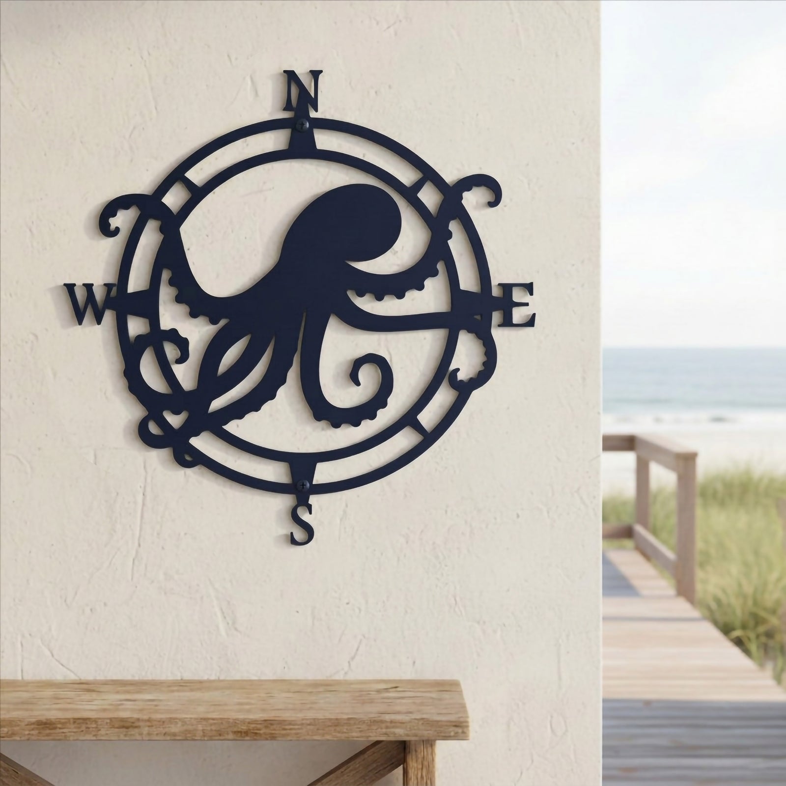 Ocean blue personalized octopus compass rose metal plaque mounted on a white exterior wall overlooking a beachside wooden boardwalk and the ocean view.