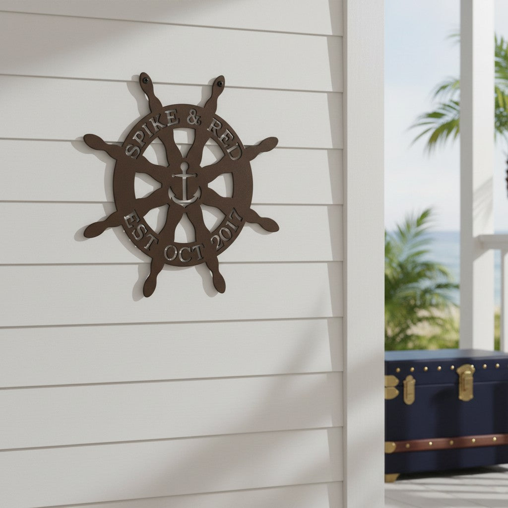 Dark brown custom metal ship wheel sign featuring a central anchor design displayed on a white outdoor wall with a tropical beach and veranda scene in the background.