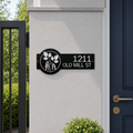 Black custom metal house number sign with elegant botanical leaf design mounted beside modern front gate and entry door displaying 1211 Old Mill St