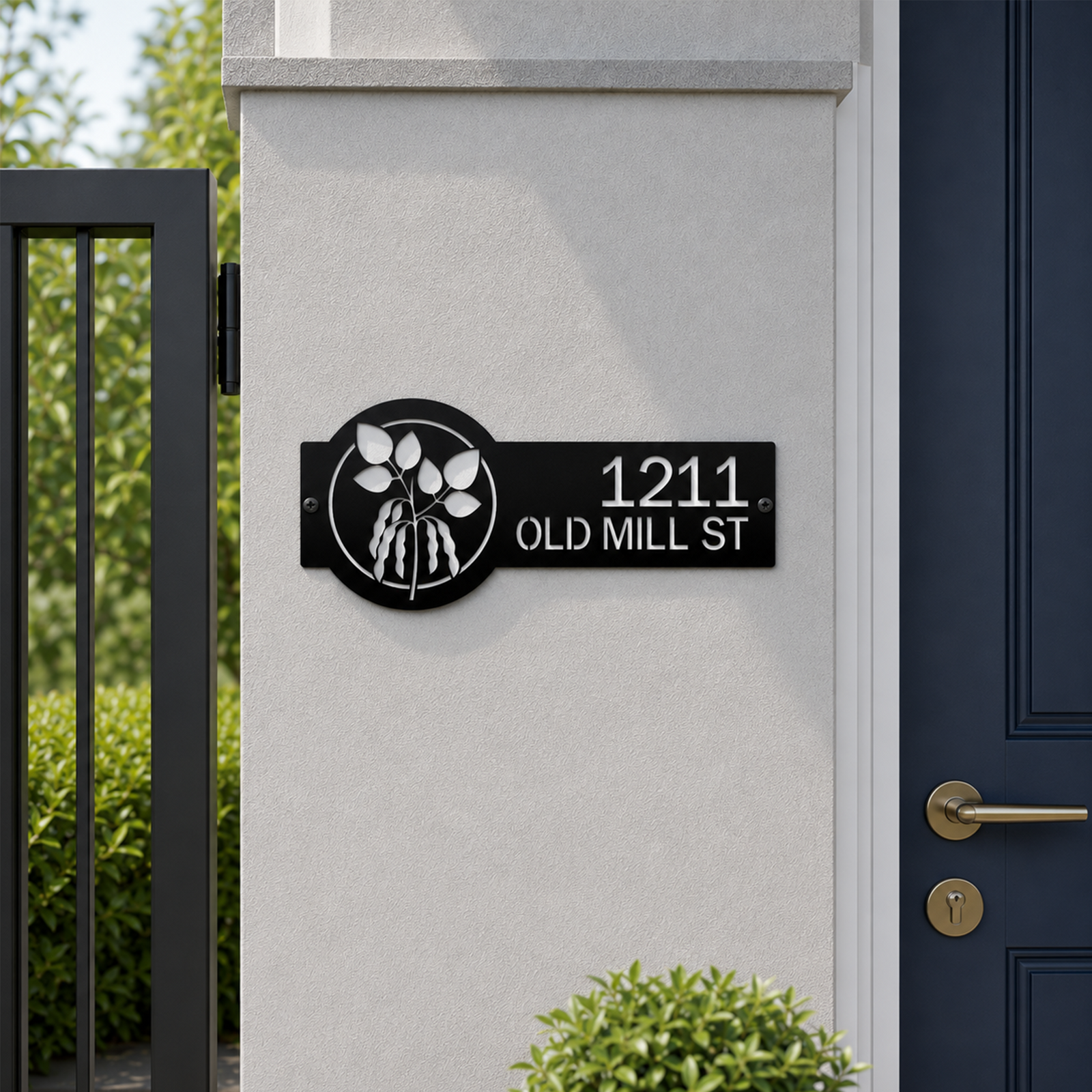 Black custom metal house number sign with elegant botanical leaf design mounted beside modern front gate and entry door displaying 1211 Old Mill St