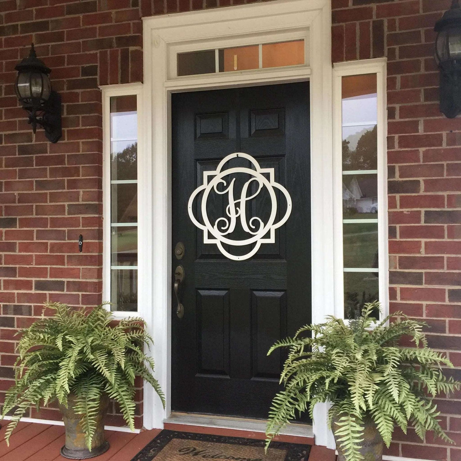 Personalized white monogram door wreath sign displayed on a black front door with brick porch entry decor