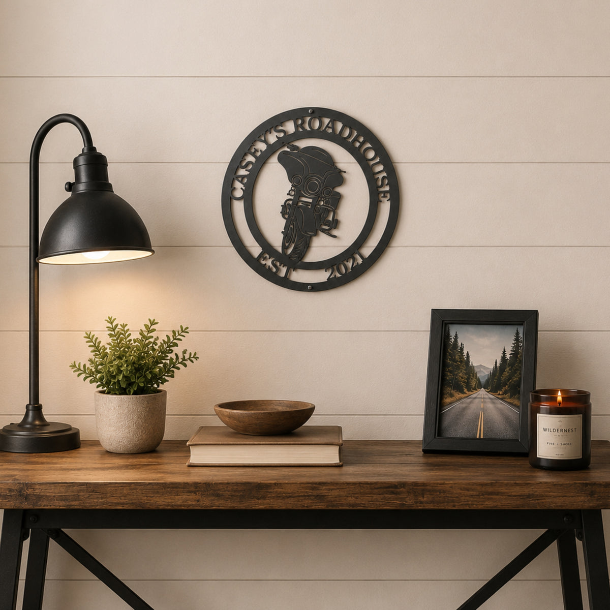 Custom motorcycle metal wall art displayed above rustic console table with lamp, candle, and framed road photo